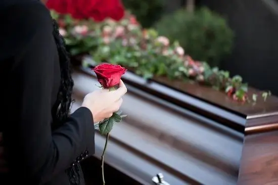 A person holding a rose in front of a casket.
