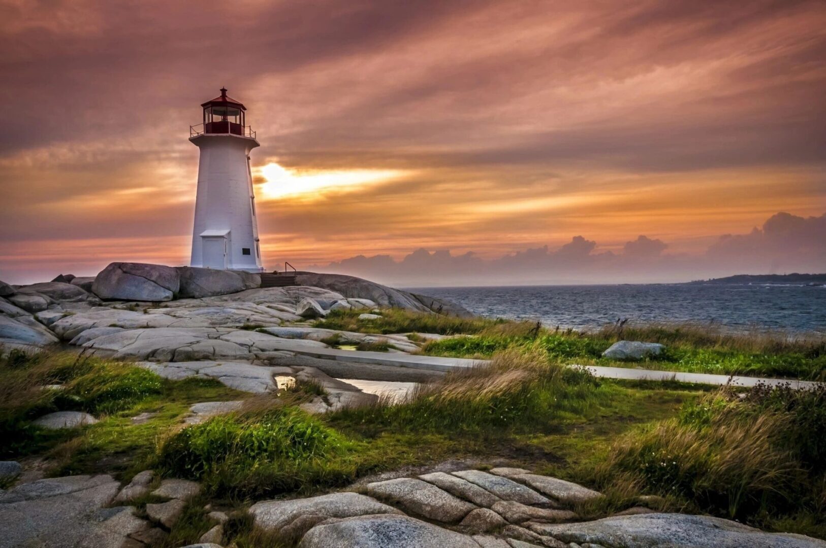 A lighthouse on the rocks at sunset.