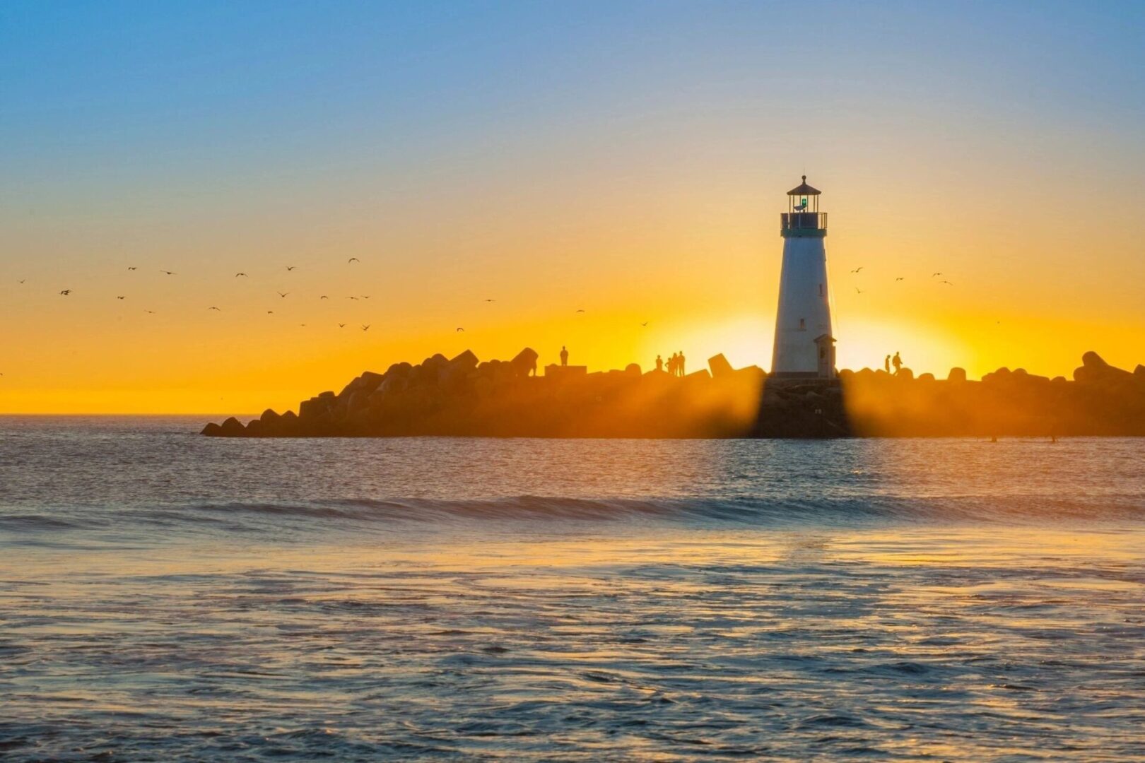 A lighthouse is shown at sunset on the water.