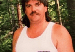 A man with long hair and a beard wearing a white shirt.