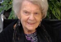 A woman with white hair sitting in front of a plant.