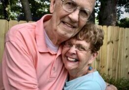 A man and woman hugging in front of a fence.