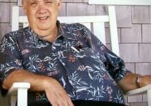 A man sitting in a chair wearing a hawaiian shirt.