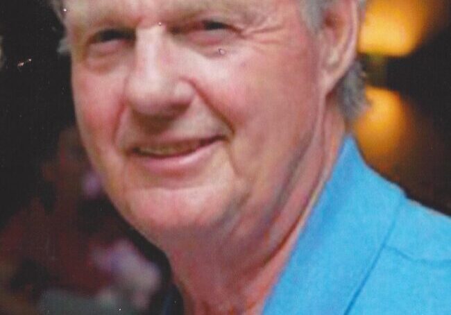 A man with grey hair and blue shirt smiling.