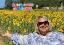 A woman standing in front of sunflowers with her arms outstretched.