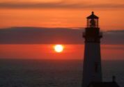 A lighthouse with the sun setting in the background.