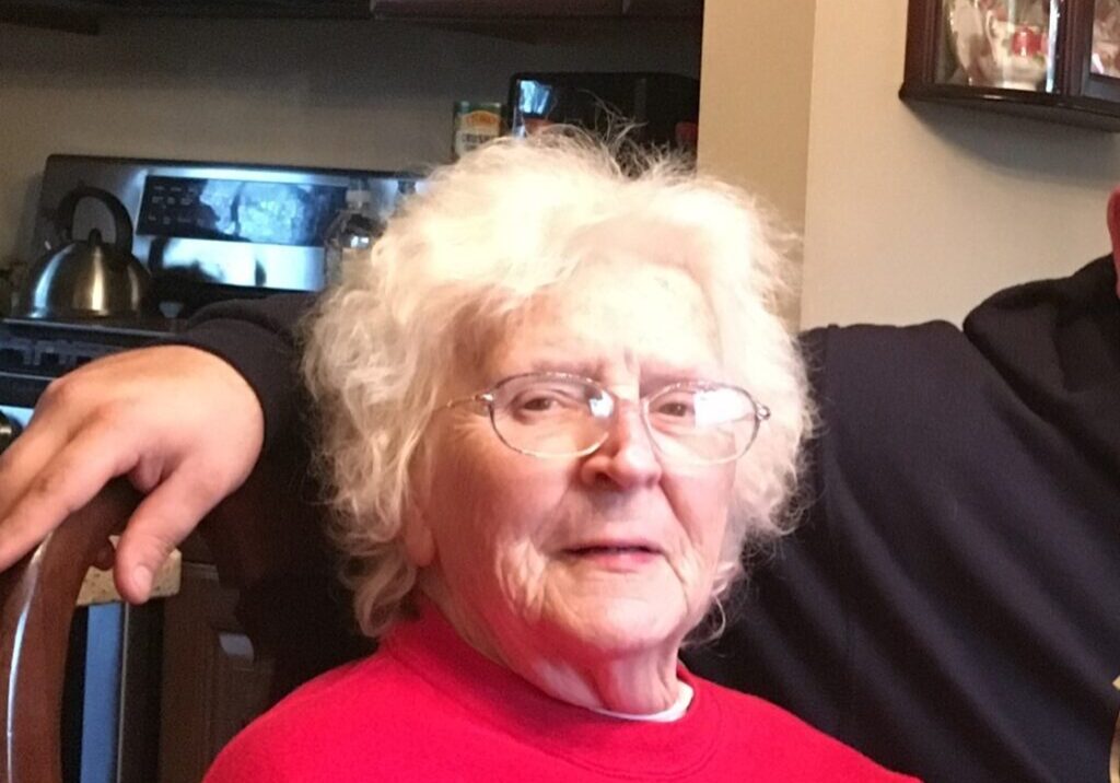 A woman with white hair and glasses in front of a tv.