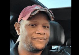 A man wearing a hat sitting in the back of a car.