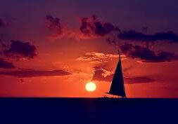 A sailboat is sailing in the ocean at sunset.