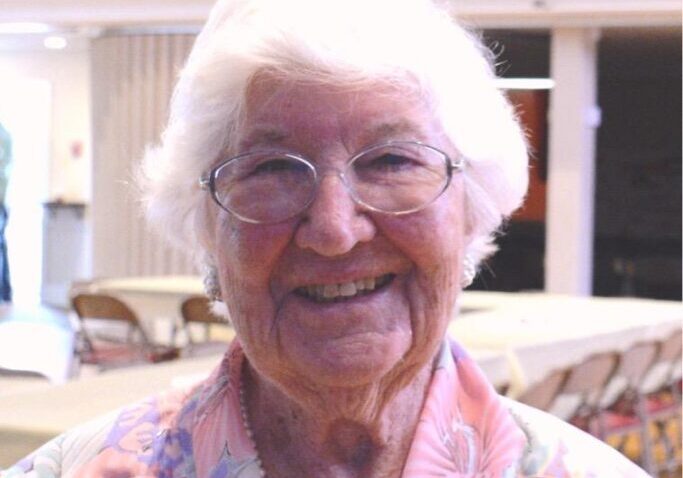 A woman with white hair and glasses smiling.