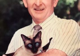 A man holding a siamese cat in his arms.