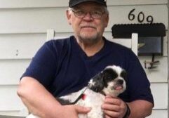 A man sitting on the porch of his home with a dog.