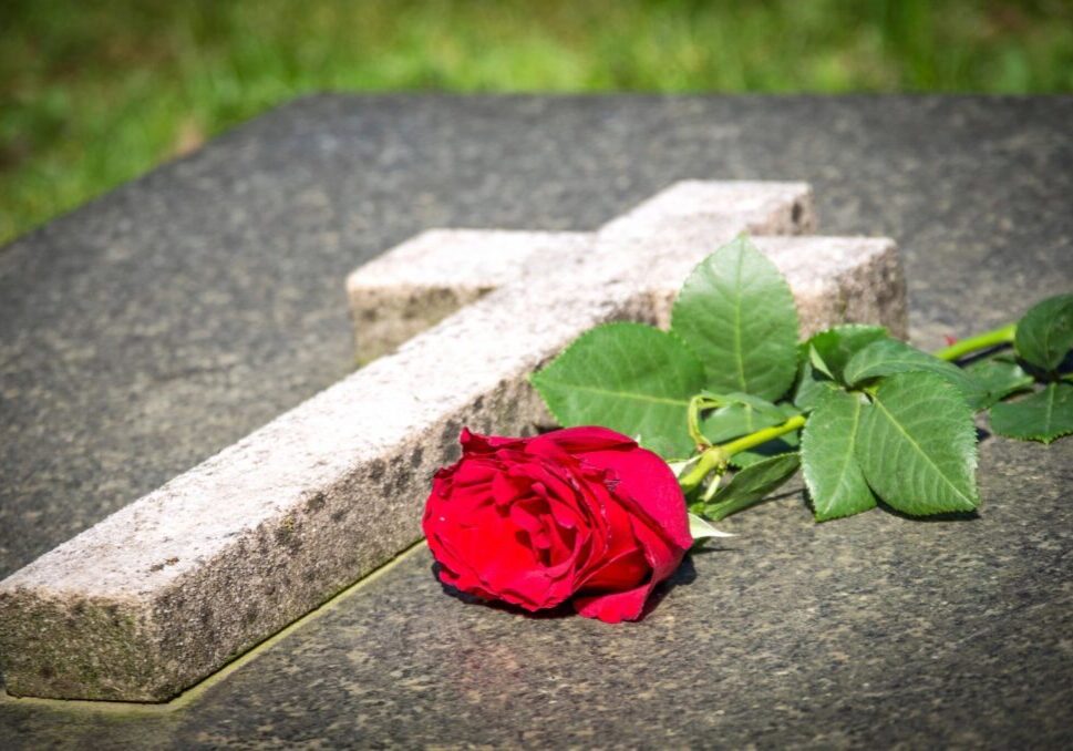 A rose laying on the ground next to a cross.