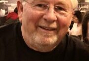 A man with white hair and glasses smiling.